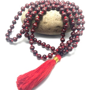 May include: A red wooden mala bead necklace with a red tassel. The beads are strung on a red cord and the tassel is attached to the end of the cord.