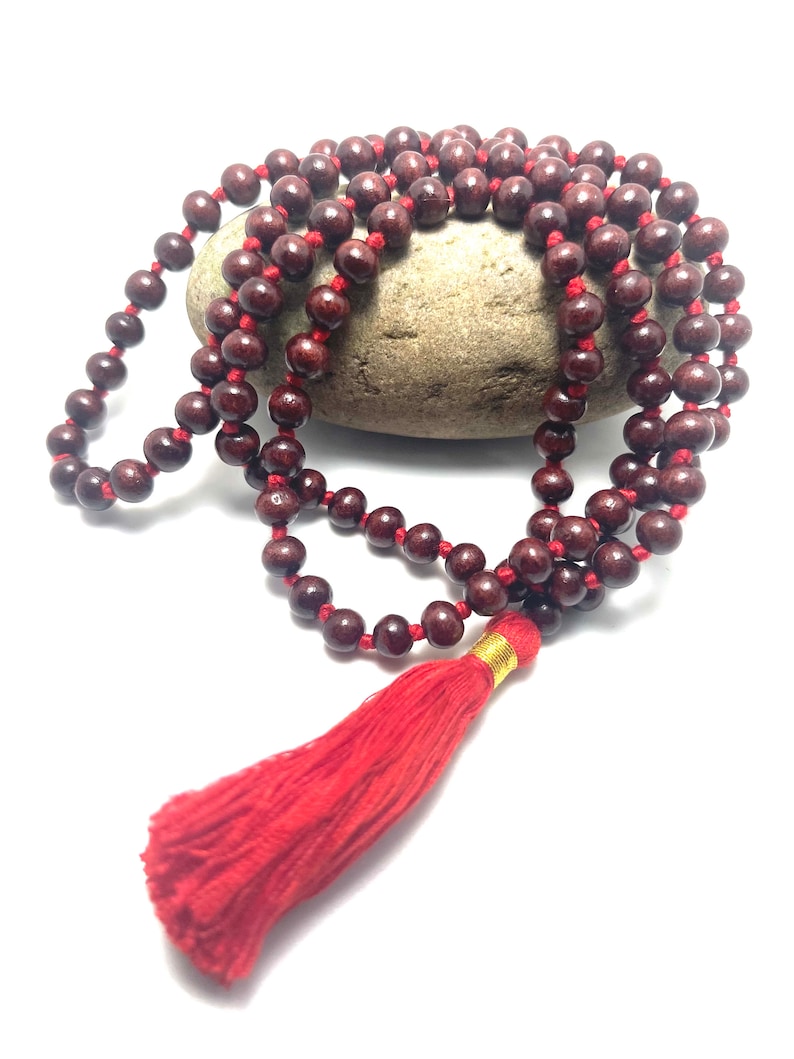 May include: A red wooden mala bead necklace with a red tassel. The beads are strung on a red cord and the tassel is attached to the end of the cord.
