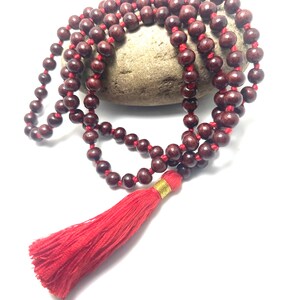 May include: A red wooden mala bead necklace with a red tassel. The beads are strung on a red cord and the tassel is attached to the end of the cord.