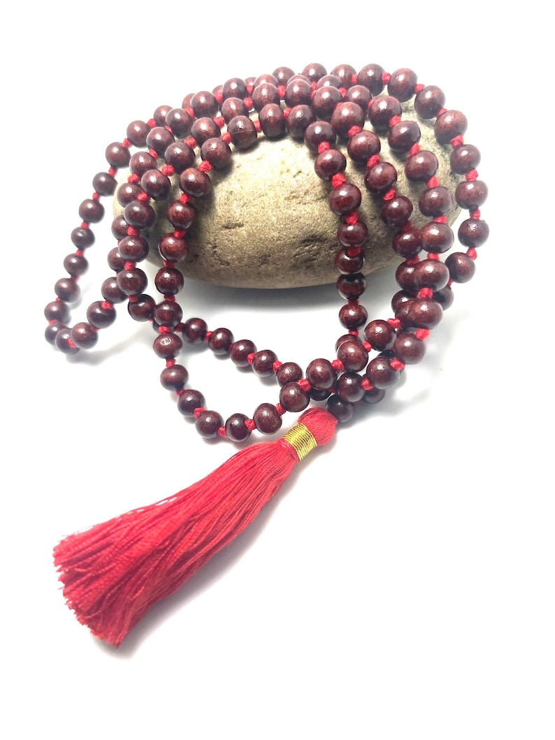 May include: A red wooden mala bead necklace with a red tassel. The beads are strung on a red cord and the tassel is attached to the end of the cord.
