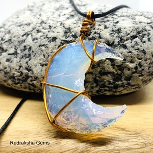 May include: A crescent moon shaped opal pendant wrapped in copper wire. The pendant is hanging from a black cord necklace.
