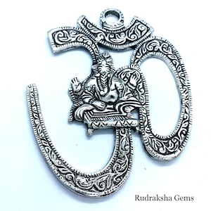 Puede incluir: Colgante de plata con símbolo Om con detalles intrincados y una representación de Ganesha en el centro. El colgante es un símbolo hindú tradicional de paz y espiritualidad.