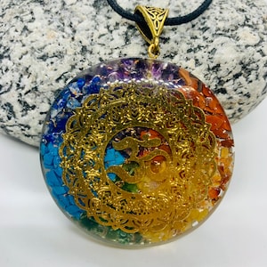 Peut inclure: Un collier pendentif rond avec un motif filigrané doré et un cordon noir. Le pendentif présente un arc-en-ciel de couleurs, dont le bleu, le vert, le jaune, l'orange et le violet, avec un symbole Om doré au centre.