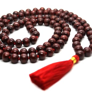 May include: A red wooden mala bead necklace with a red tassel. The beads are round and have a smooth finish.