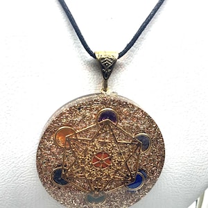 May include: A round pendant necklace with a gold-colored Metatron's Cube design. The pendant has a gold-colored bail and is suspended from a black cord. The pendant is a mix of gold and brown with colorful gemstones.