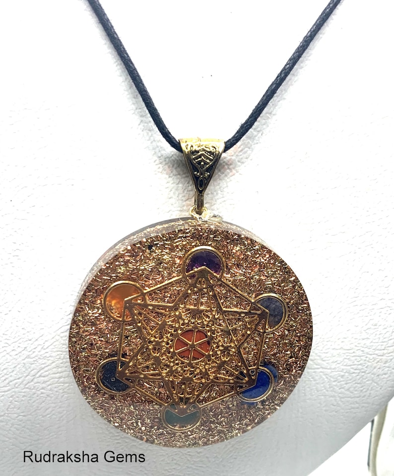 May include: A round pendant necklace with a gold-colored Metatron's Cube design. The pendant has a gold-colored bail and is suspended from a black cord. The pendant is a mix of gold and brown with colorful gemstones.