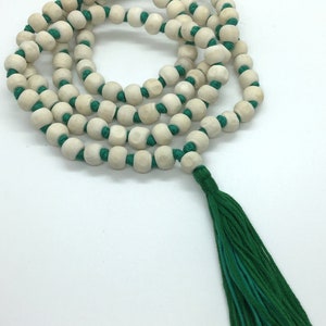 May include: A string of light-coloured, round wooden beads knotted onto a vibrant green cord, arranged in a circular pattern. The necklace features a long, matching green tassel at the end. The text Rudraksha Gems is printed in the bottom corner.
