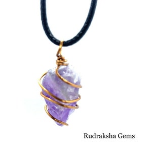 Puede incluir: Un collar con un colgante de cristal de amatista púrpura envuelto en alambre dorado. El collar es de diseño simple, con un solo colgante de cristal. El cristal es una amatista natural de corte tosco, con un hermoso color púrpura.