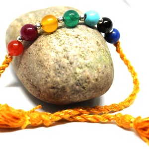 May include: A yellow braided cord bracelet with seven colorful beads. The beads are red, orange, yellow, green, blue, black, and turquoise.