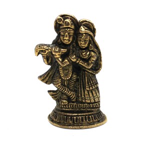 Puede incluir: Una figurita de metal de color dorado de una pareja, probablemente representando a Radha y Krishna, de pie juntos. La figurita est&aacute; detallada con intrincados tallados y est&aacute; colocada sobre una base circular.