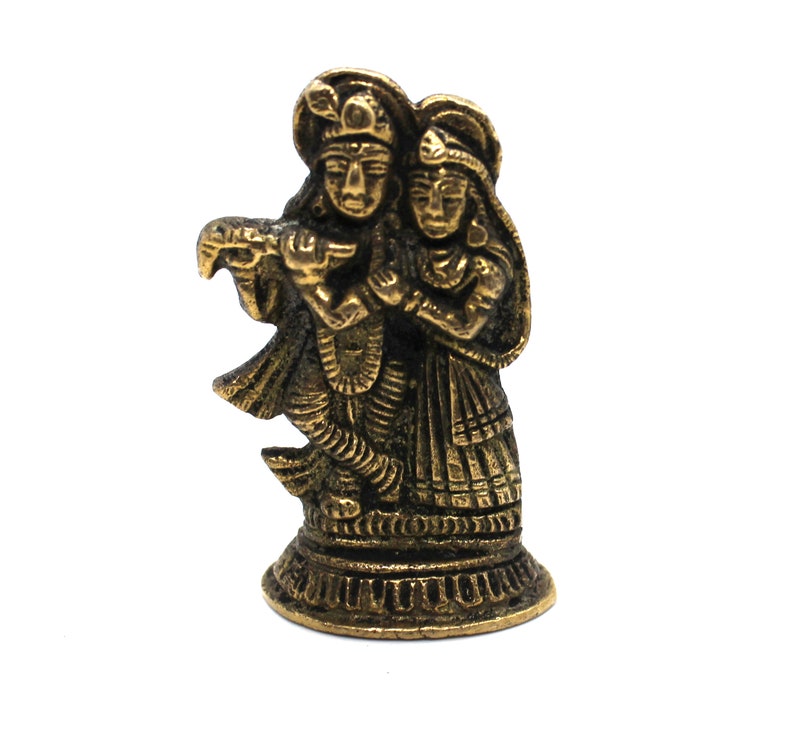 Puede incluir: Una figurita de metal de color dorado de una pareja, probablemente representando a Radha y Krishna, de pie juntos. La figurita est&aacute; detallada con intrincados tallados y est&aacute; colocada sobre una base circular.