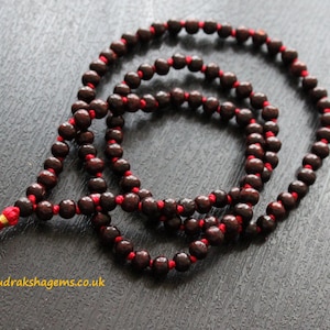 May include: A dark brown wooden mala with red string and a red tassel. The mala has 108 beads and is used for meditation and prayer.