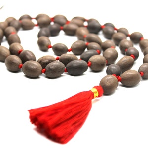 May include: A brown wooden mala bead necklace with a red tassel. The beads are strung on a red cord.
