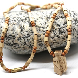 May include: A handcrafted wooden necklace featuring a pendant with carved geometric designs. The necklace is composed of light brown rectangular beads and smaller, round, darker brown beads. A brass clasp secures the necklace.