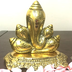 Puede incluir: Una estatua dorada de Ganesh de lat&oacute;n con detalles intrincados. La estatua presenta a Ganesh sentado con una cabeza grande, adornada con tres gemas rojas. La base es ornamentada y el dise&ntilde;o es muy detallado.