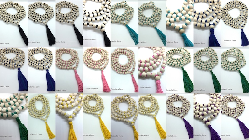 May include: A collection of twenty-four mala bead necklaces arranged in a grid. Each necklace consists of light-coloured wooden beads strung together with coloured thread, featuring a matching fabric tassel at the end of each strand.