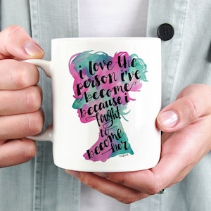 May include: White ceramic mug with a watercolor silhouette of a woman's head and the text "I love the person I've become because I fought to become her."