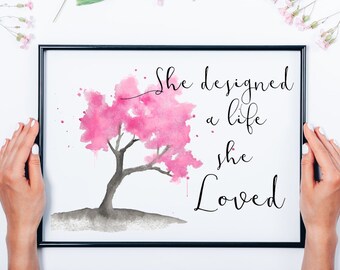 Puede incluir: Una impresión enmarcada con una pintura de acuarela de un árbol rosa con el texto "She designed a life she Loved".