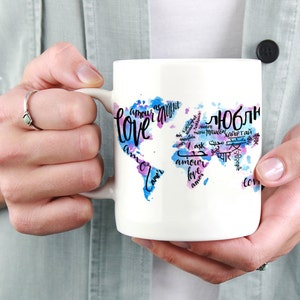 May include: White ceramic mug with a watercolor world map design. The map is decorated with the word "love" in different languages, including "amor", "amour", "liebe", "amore", "miłość", "amor", and "愛".