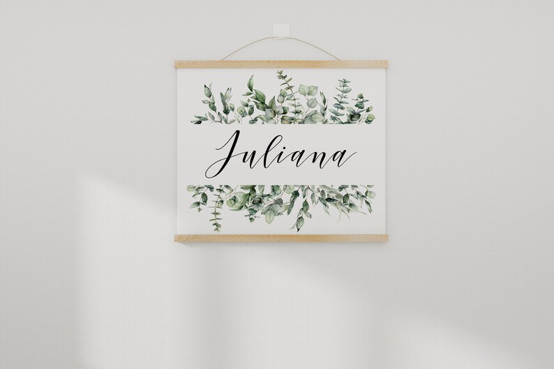 May include: A white canvas print with a wooden frame, featuring a green watercolor floral design and the name "Juliana" in black calligraphy.
