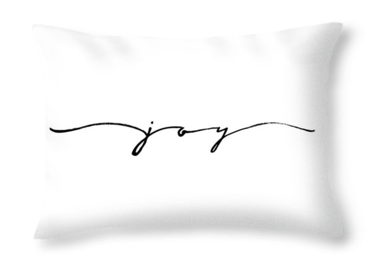 May include: White throw pillow with the word "joy" in black cursive script. The word is centered horizontally and slightly below the center of the pillow. The pillow has a soft, inviting appearance.