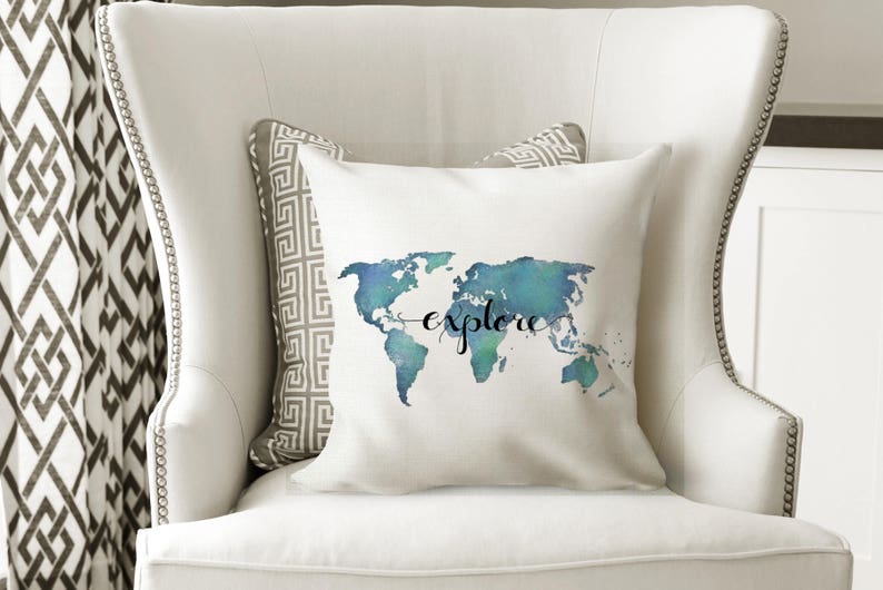 K&ouml;nnte beinhalten: Ein wei&szlig;es Kissen mit einem Aquarell-Weltkarten-Design in Blaut&ouml;nen und Gr&uuml;n. Das Wort "explore" ist in schwarzer Kursivschrift &uuml;ber die Karte geschrieben.