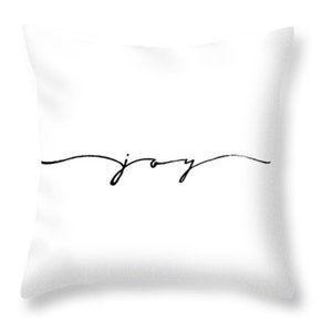 May include: White square throw pillow with the word "joy" written in a black, cursive font. The word is centered horizontally and sits on a single, thin, curved line.