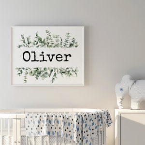May include: A white framed print with a watercolor illustration of green leaves and the name "Oliver" in black text.