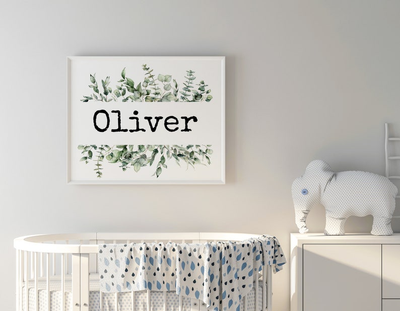 May include: A white framed print with a watercolor illustration of green leaves and the name "Oliver" in black text.