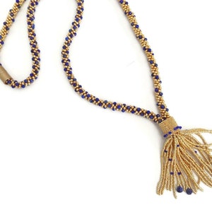 May include: A gold and blue beaded necklace with a tassel. The necklace is made of small, round beads and has a gold clasp.