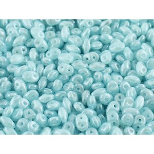 May include: A close-up view of a large quantity of light blue seed beads. The beads are oval shaped with a hole in each end. The beads have a slightly iridescent finish.