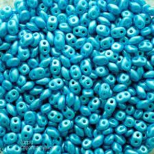 May include: A close-up view of a large quantity of turquoise blue seed beads. The beads are small and oval-shaped with two holes.
