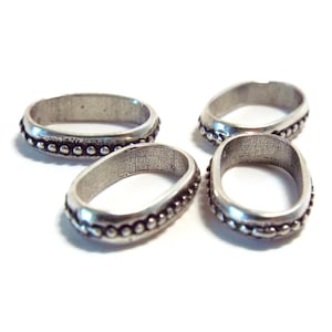 May include: Four silver oval-shaped rings with a beaded edge. The rings are arranged in a semi-circle.