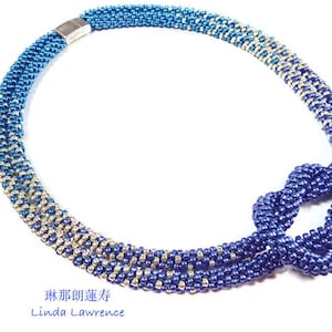 Op de afbeelding: Een blauwe, zilveren en witte kralenketting met een knoop aan het einde. De ketting is gemaakt van kleine, ronde kralen en heeft een zilveren sluiting. De tekst "Linda Lawrence" is onder de ketting gedrukt.