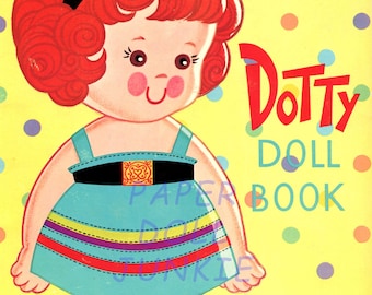 Op de afbeelding: Een vintage papieren poppenboek met Dotty, een roodharig meisje met een blauwe jurk en zwarte schoenen. Het boek bevat kartonnen uitknipbare jurken, hoeden en schoenen. De omslag heeft een kleurrijk stippenpatroon.