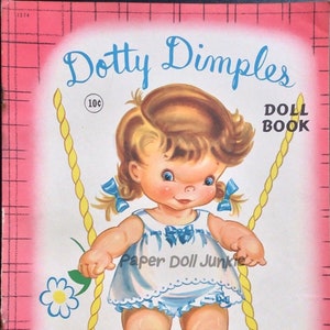 Puede incluir: Un libro de muñecas de papel vintage con Dotty Dimples, una niña con cabello rubio y ojos azules, vestida con un vestido azul y blanco y sosteniendo una cuerda de columpio amarilla. La portada del libro es rosa con un patrón de cuadrícula y el texto "Dotty Dimples Doll Book 10c" está impreso en la parte delantera.