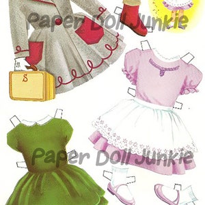 Puede incluir: Un conjunto de mu&ntilde;eca de papel con una ni&ntilde;a con un vestido rosa y un delantal blanco, un vestido verde, un abrigo gris con detalles rojos, un sombrero y zapatos. La mu&ntilde;eca sostiene una varita m&aacute;gica y est&aacute; rodeada de brillo.