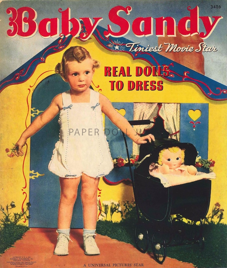 Może przedstawiać: Antyczna książka z papierowymi lalkami przedstawiająca Baby Sandy, "najmniejszą gwiazdę filmową", z lalką w w&oacute;zku. Okładka zawiera kolorową ilustrację domu w niebiesko-ż&oacute;łtej kolorystyce. Tekst "Real Dolls to Dress" jest wyraźnie widoczny.