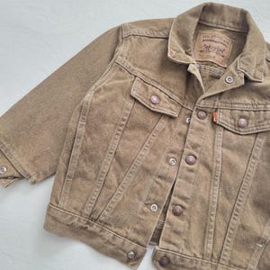May include: A brown denim jacket with a button-up front, two chest pockets, and two side pockets. The jacket has a classic collar and features the Levi Strauss & Co. label. The jacket has a vintage look.