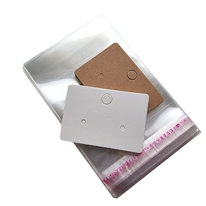 May include: A stack of clear plastic bags with a white and brown card with holes for earrings. The bags have pink text that says "STUD EARRING"