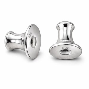 May include: Two shiny silver earring backs. Each back has a flat, round base with the number "925" stamped on it. The post is a rounded, cylindrical shape. The earring backs are designed to secure earrings.