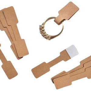 May include: A set of brown paper ring tags with a white adhesive strip. The tags are designed for hanging jewellery, such as rings, necklaces, or bracelets.