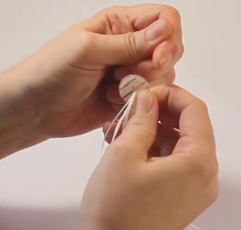 May include: A hand holding a white button with a black and white striped design. The button has a loop of white thread attached to it.