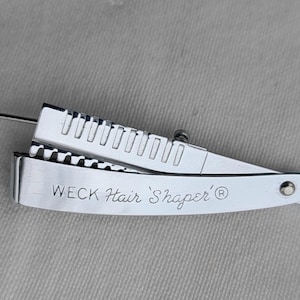 May include: A silver hair shaper with a comb and a blade. The shaper has the text "WECK Hair 'Shaper' ®" engraved on it.