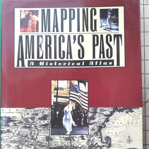 Puede incluir: Un libro de tapa dura titulado "Mapping America's Past: A Historical Atlas". La portada es de color burdeos con imágenes y texto. El título está en letras negras grandes. El libro presenta mapas e ilustraciones históricas.