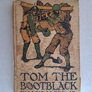Könnte beinhalten: Vintage Buchcover mit einer Baseballszene mit zwei Spielern in Aktion. Der Titel "TOM THE BOOTBLACK" ist deutlich zu sehen, darunter der Name des Autors. Das Cover hat einen beigen Hintergrund mit Illustrationen in Braun-, Grün- und Orangetönen.