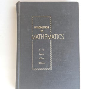 May include: A vintage, dark grey book titled "Introduction to Mathematics." The title and author names are in gold lettering within a decorative border. The book's cover shows signs of wear, suggesting its age.