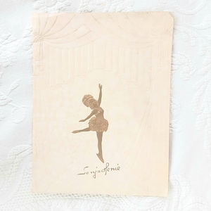 May include: Vintage beige postcard featuring a ballerina in a tutu, with one leg extended and arms raised. The dancer is in a graceful pose, with the name "Sonja Henie" written in cursive below. The background has a decorative design.