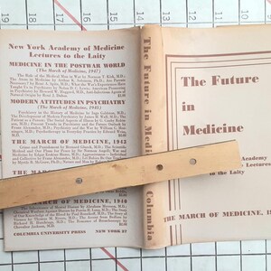 May include: An open book titled "The Future in Medicine" with a wooden ruler across the pages. The book's cover and pages display text about medicine, including "New York Academy of Medicine" and "The March of Medicine, 1949."