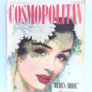 May include: Vintage Cosmopolitan magazine cover from December 1949. The cover features a woman with dark hair, red lipstick, and a floral headpiece. The magazine title is in large pink letters. Text includes "HERE'S ADDIE" and "A Letter to Five Wives."